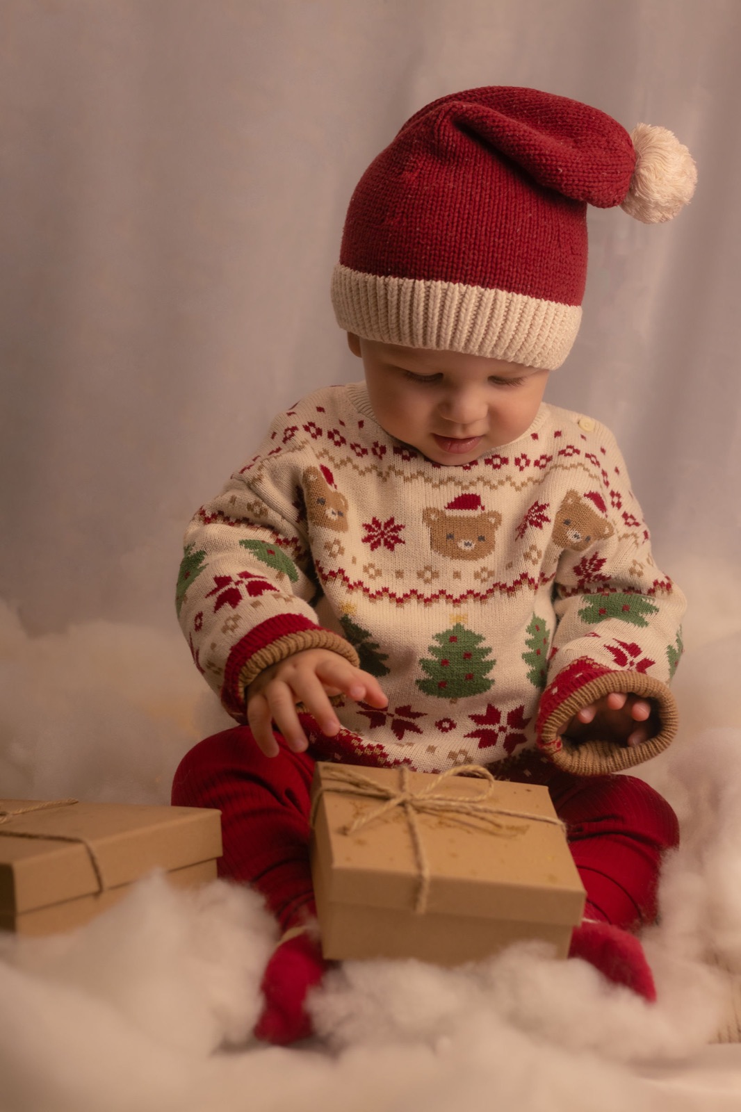 Baby in Weihnachtsmütze packt ein Geschenk aus