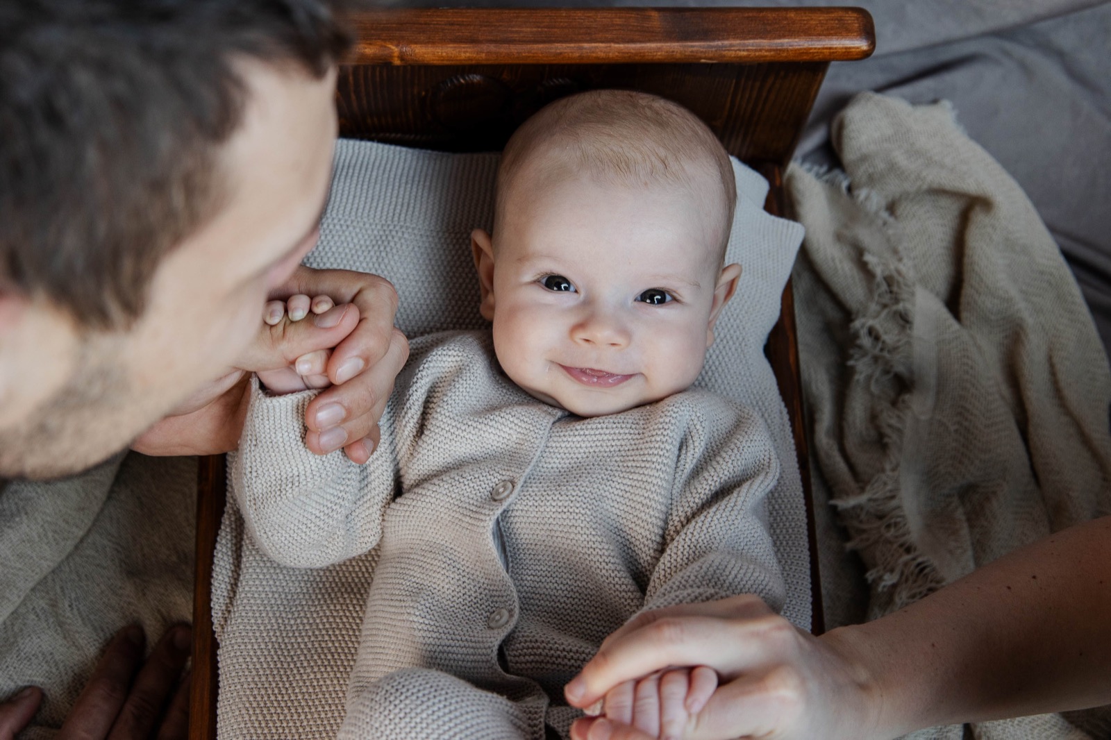 Baby lächelt zwischen den Händen der Eltern
